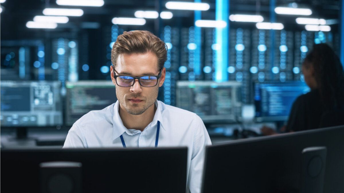 Man working at computer monitors in a data center with illuminated server racks