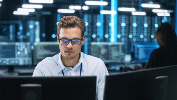 Man working at computer monitors in a data center with illuminated server racks